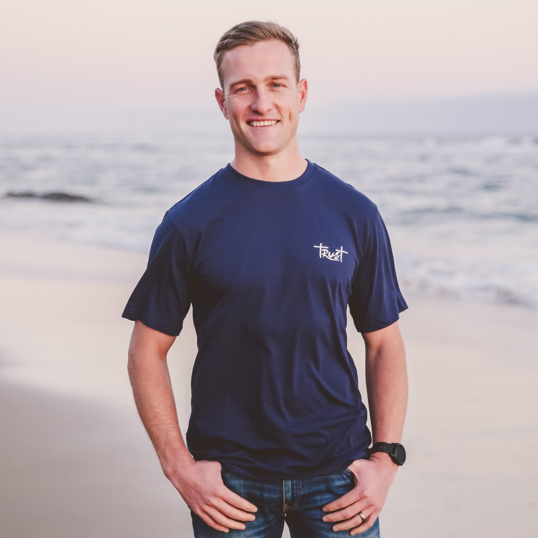 Man wearing a Navy Christian T-shirt with the word: "Trust", standing on the beach.