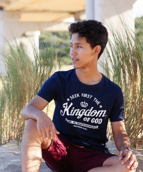Young man on beach wearing navy blue Christian T shirt with white words 